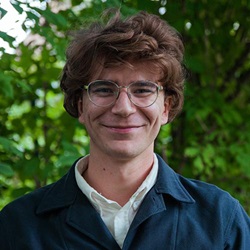 Head and shoulders image of man with glasses in white shirt and blue jacket in front of trees