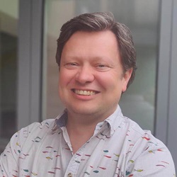 Head and shoulders image of man in white shirt with coloured flecks